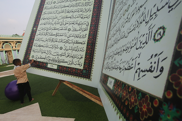 Seorang anak membaca replika Al-Quran raksasa di halaman Masjid Al-Azhom, Kota Tangerang, Banten, Selasa (9/7/2024). (Foto: Edwin B/ Muslim Obsession)