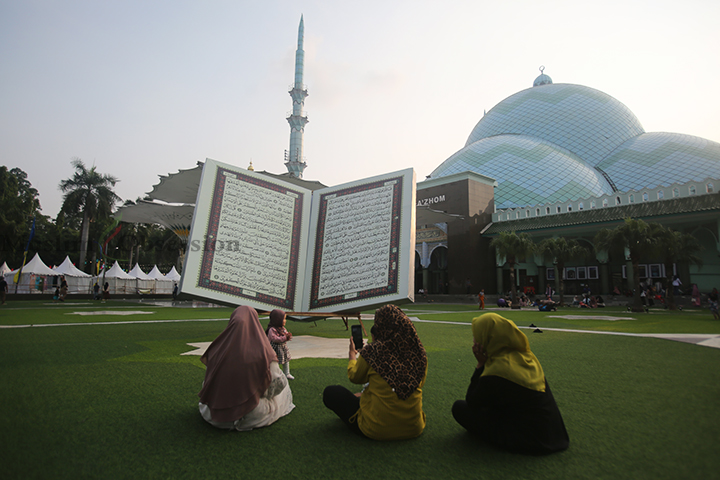 Sejumlah pengunjung sedang santai di depan replika Al-Quran raksasa di halaman Masjid Al-Azhom, Kota Tangerang, Banten, Selasa (9/7/2024). (Foto: Edwin B/ Muslim Obsession)