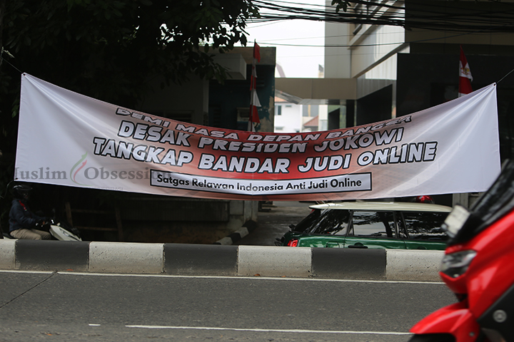 Sejumlah kendaraan melintasi spanduk yang bertuliskan desakan kepada Presiden Jokowi untuk menangkap bandar Judi Online (Judol) yang terpasang di Jalan Sultan Iskandar Muda, Arteri Pondok Indah, Jakarta Selatan, Kamis (8/8/2024). (Foto: Edwin B/ Muslim Obsession)