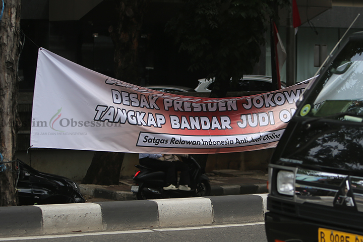 Sejumlah kendaraan melintasi spanduk yang bertuliskan desakan kepada Presiden Jokowi untuk menangkap bandar Judi Online (Judol) yang terpasang di Jalan Sultan Iskandar Muda, Arteri Pondok Indah, Jakarta Selatan, Kamis (8/8/2024). (Foto: Edwin B/ Muslim Obsession)