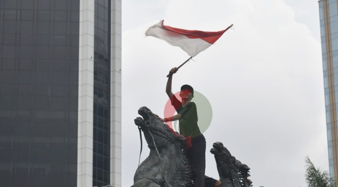 Seorang pelajar memasang bendera merah putih di patung kuda Jakarta, Selasa (20/10/2020)